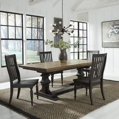 a dining room table with four chairs and a vase on the rug in front of it