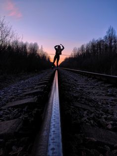 a person standing on train tracks with their arms outstretched in front of the sun setting