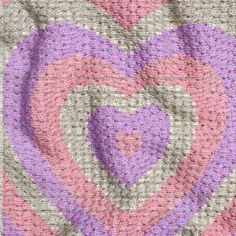 a knitted heart is shown in pink, purple and grey colors on a gray background