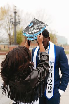 a man and woman kissing each other while holding a graduation cap over their heads in front of them