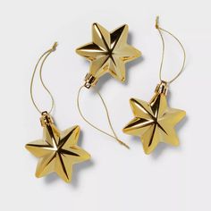 three gold stars are hanging from chains on a white surface, one is shaped like an ornament and the other is shaped like a star