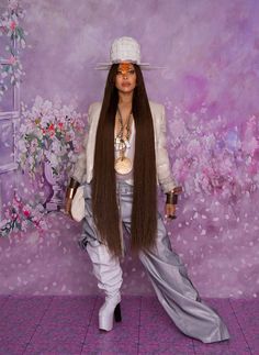 a woman with long brown hair standing in front of a purple wall wearing a white hat