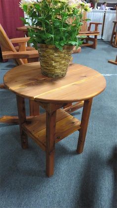 a wooden table with a basket full of flowers on it's top and two chairs in the background