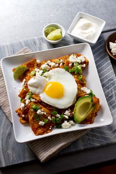 a square white plate topped with fried eggs and avocado next to sour cream