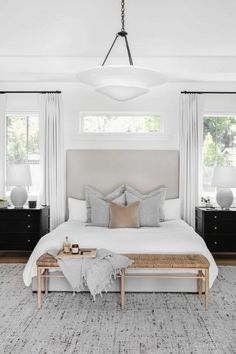 a bedroom with white walls and gray carpeted flooring, large bed in front of two windows