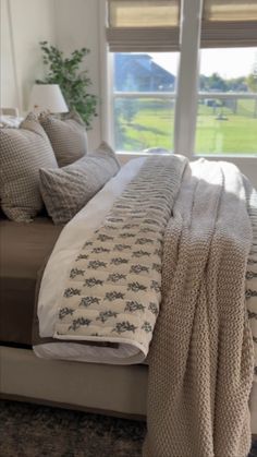 a bed sitting in front of a window covered in blankets and pillows on top of it