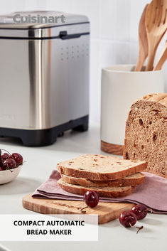 a loaf of bread sitting on top of a cutting board next to a bowl of cherries