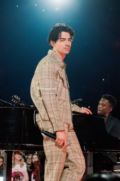 a man in a suit standing next to a piano on stage with people behind him