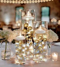 candles and flowers are arranged in glass vases on a table with lights behind them