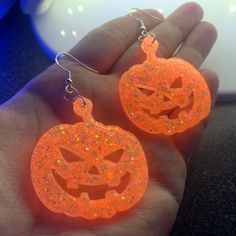 Each pair of neon orange jack-o-lantern earrings are handmade to order, therefore no two sets are identical! Every resin jewelry piece is slightly unique and one of a kind. However, I try to get as close to the photos as possible :) Made with sterling silver plated fishhook earrings (clear rubber backing included). Hypoallergenic & nickel-free. Each pumpkin is approximately 1.5" x 1.75" and are made with epoxy resin and holographic neon orange glitter. UV blacklight reactive.  Perfect for Hallow Fun Orange Earrings For Halloween, Fun Orange Halloween Earrings, Fun Orange Jewelry For Halloween, Fun Orange Halloween Jewelry, Novelty Orange Earrings For Halloween, Orange Novelty Halloween Jewelry, Spooky Orange Halloween Jewelry, Spooky Orange Jewelry Gift, Spooky Orange Jewelry For Gifts