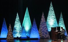 a man is sitting at a piano in front of christmas trees with lights on them