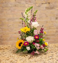 a bouquet of flowers sitting on top of a counter next to a brick wall in the background