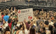 a large group of people standing in front of a stage holding signs that read harry please gesture so i can move on