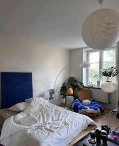 a bed room with a neatly made bed next to a window and a lamp hanging from the ceiling