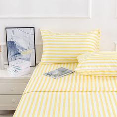 a yellow and white striped bed spread on a nightstand next to a framed photograph in a bedroom