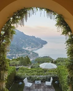 an outdoor dining area with chairs and umbrellas overlooking the sea, mountains and greenery