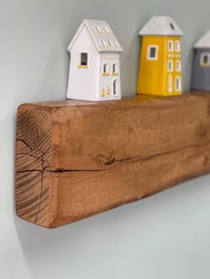 three small houses are on top of a wooden shelf with white and yellow painted houses