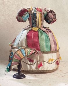 an old fashioned hat is sitting on top of a small black stand and has colorful fabric around it