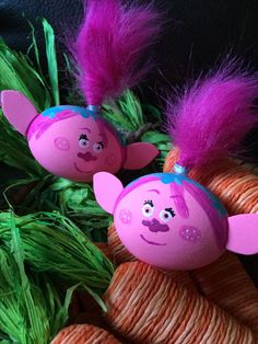 two pink troll dolls sitting on top of some green grass with purple feathers around them