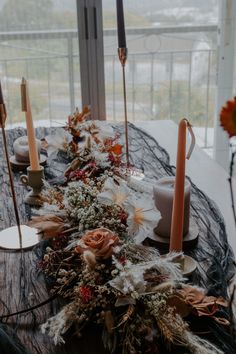 a table with candles, flowers and other items on it in front of a window