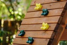 a wooden play structure with green and yellow plastic toys on it's sides, along with trees in the background