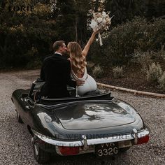 a bride and groom are sitting in the back of a convertible car with their arms up