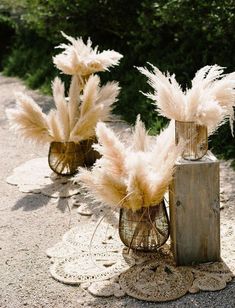 two vases filled with feathers sitting on top of a doily covered ground next to trees