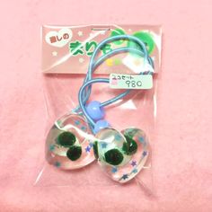 two ear buds in plastic packaging on a pink surface with white stars and blue string