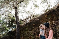 a woman holding a small child in her arms while standing next to a rock wall