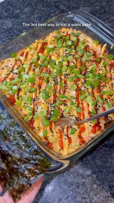 someone is holding a spoon over a casserole in a glass dish with green onions and carrots