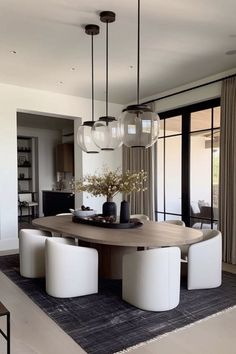 a dining room table with four chairs and a vase on top of it in front of large windows