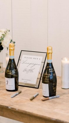 two bottles of champagne sitting on top of a wooden table next to candles and flowers