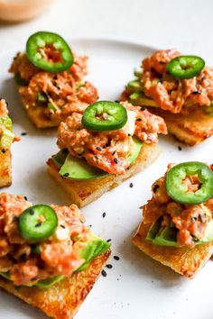 small pieces of bread topped with meat and veggies on top of a white plate