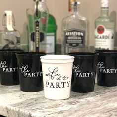 four black cups sitting on top of a counter with liquor bottles in the back ground