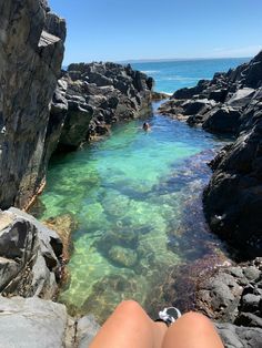 a person laying on top of a rocky beach next to the ocean with their feet in the water