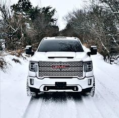 a white gmc truck driving down a snow covered road with trees in the background