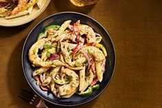 a plate of pasta with shrimp and vegetables on it next to a glass of wine