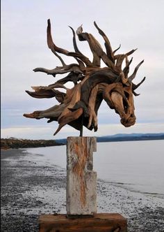 a sculpture made out of driftwood sitting on top of a wooden block next to the ocean