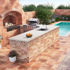 an outdoor kitchen next to a pool with a grill and sink on it's side