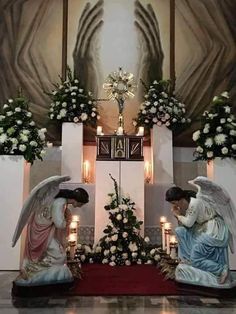 two angel statues sitting next to each other in front of a wall with flowers and candles