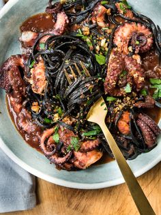 an octopus dish with pasta and sauce in a white bowl on a wooden table next to a fork