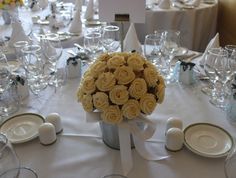 a bouquet of yellow roses sits on top of a table set for a formal dinner