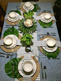 the table is set with plates, silverware and green plants