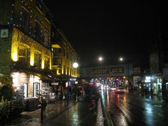 a city street at night with people walking on the sidewalk and cars driving down it