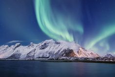 the northern lights shine brightly in the sky above snow covered mountains and lake with water below