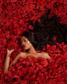 a woman laying in red flowers with her hair up and eyes closed, surrounded by petals