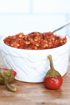 a white bowl filled with food sitting on top of a wooden table next to two peppers