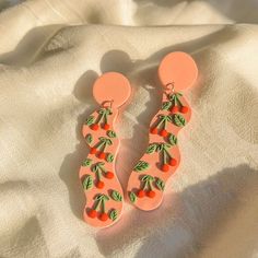 two pairs of earrings with cherries on them sitting on top of a white sheet