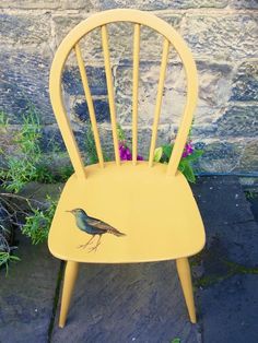 a yellow chair with a small bird painted on it's back sitting in front of a stone wall