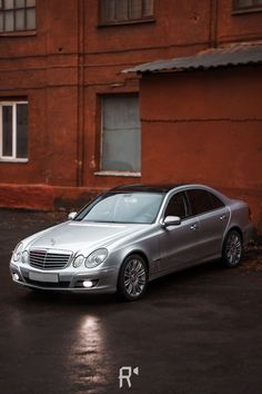 a silver car parked in front of a red building on a wet parking lot next to a fire hydrant